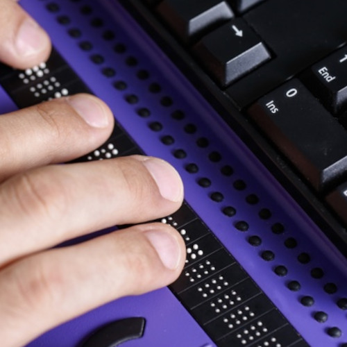 Dedos sobre un teclado Braille. También aparece un teclado de computador